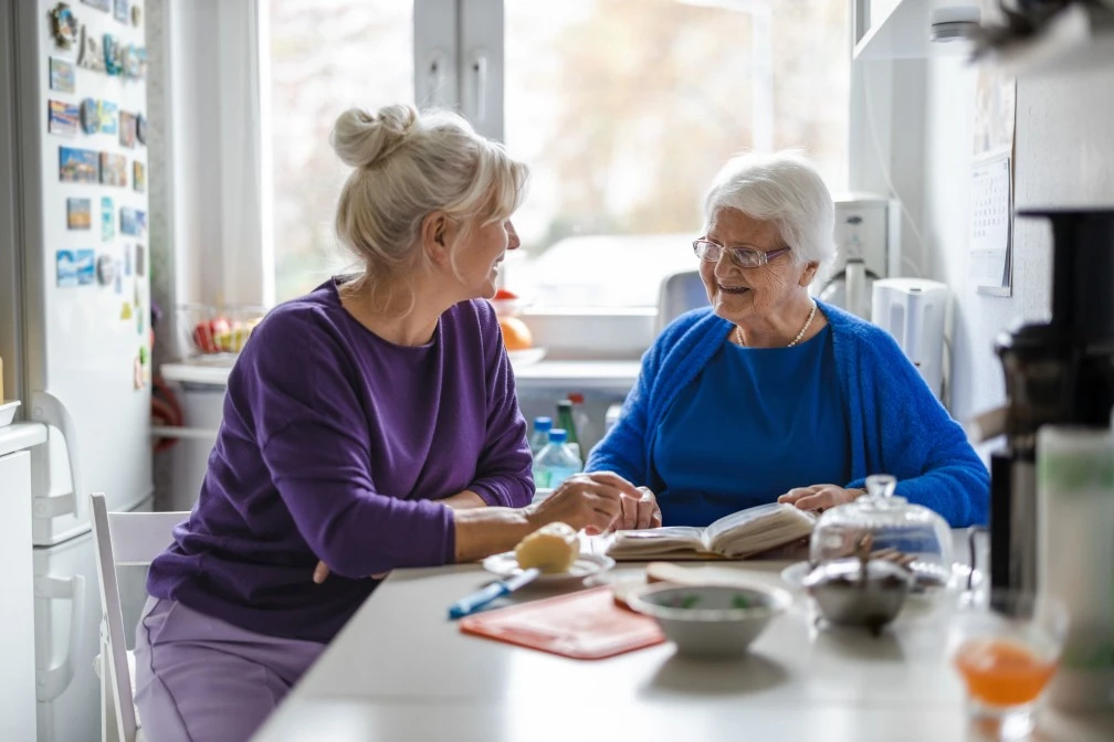 Happy woman with elderly woman at home reading a book together