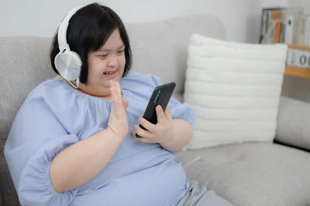 Happy disabled woman with down syndrome on video call on mobile and waving at phone