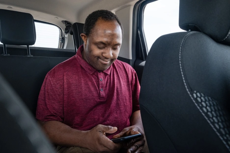 Disabled man in back of car smiling and looking at phone