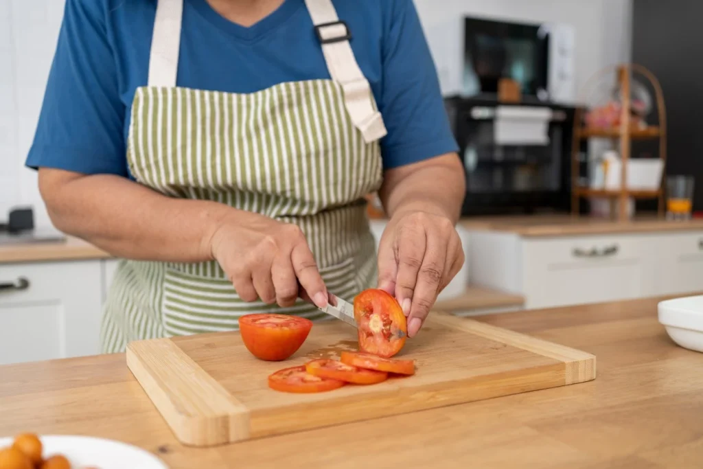 Close up of person chopping tomatoes on chopping board in kitchen