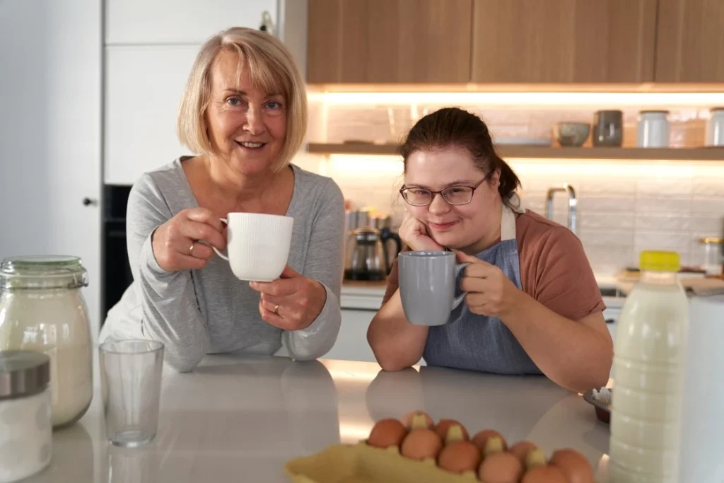 Disabled woman with down syndrome in kitchen with support worker sharing a cup of tea