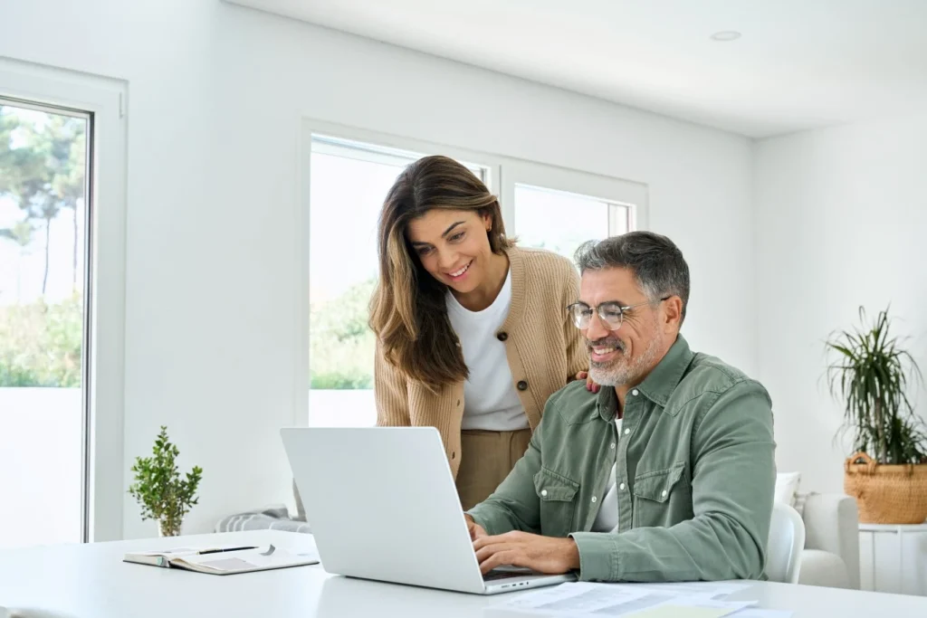 Happy couple at desk at home using laptop to make an NDIS referral