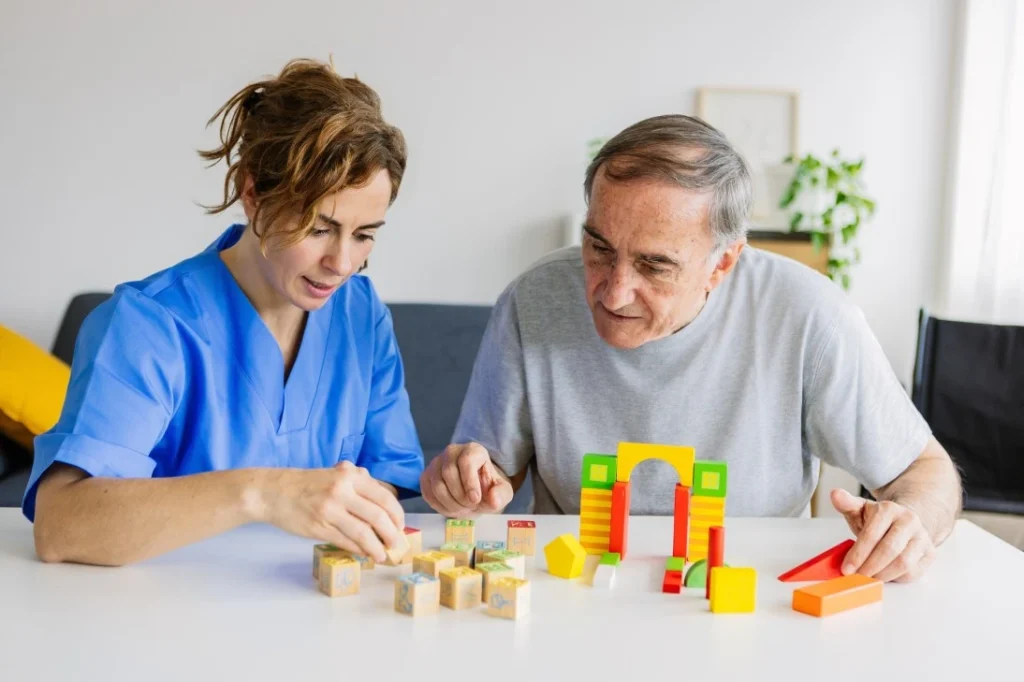 Elderly man sitting with nurse doing an activity with wooden blocks